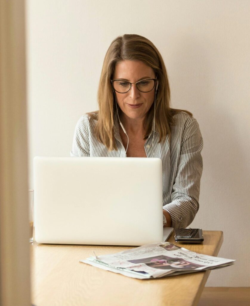 Businesswoman working remotely on a laptop at home, enjoying natural light in a modern, minimalist setting.